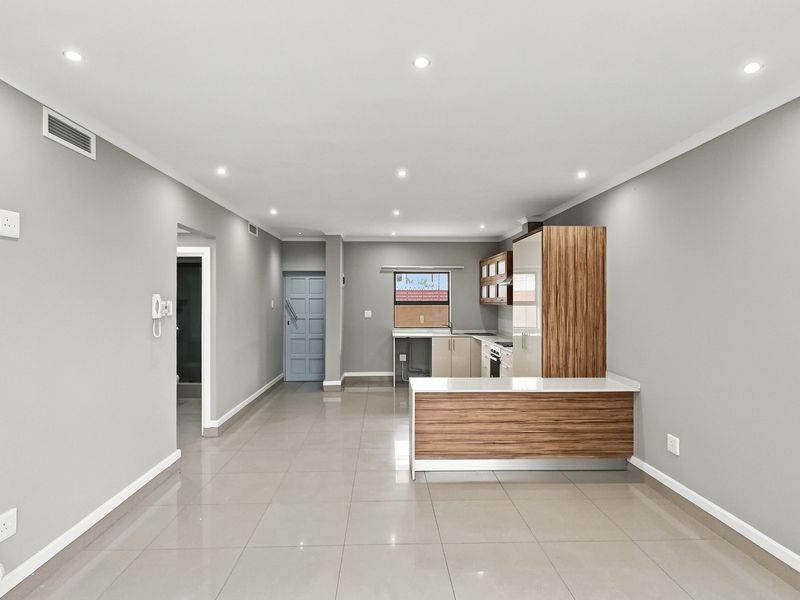 Spacious open-plan living and kitchen area featuring modern cabinetry, a central island, tiled flooring, and recessed lighting in a neutral, well-maintained apartment setting.