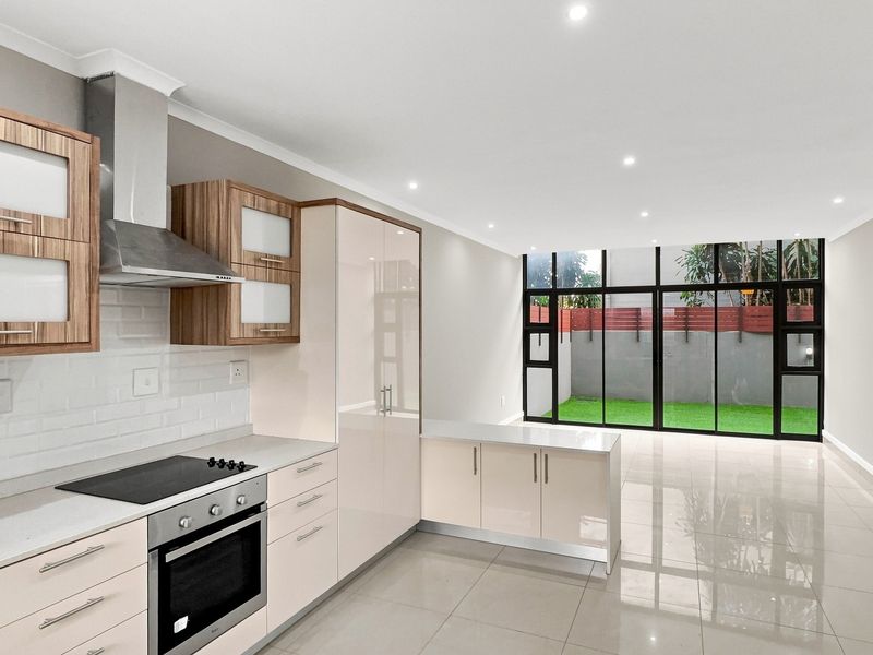 Modern open-plan kitchen featuring sleek cabinetry, integrated appliances, and high-gloss floor tiles, flowing seamlessly into a bright living area with large glass doors.