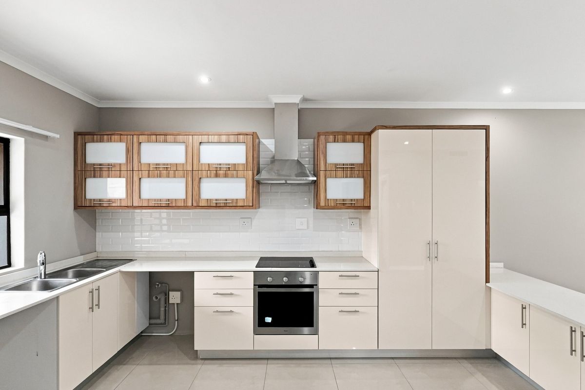 Modern kitchen featuring sleek cabinetry, stone countertops, subway tile backsplash, and integrated stainless steel appliances including an oven and extractor fan.