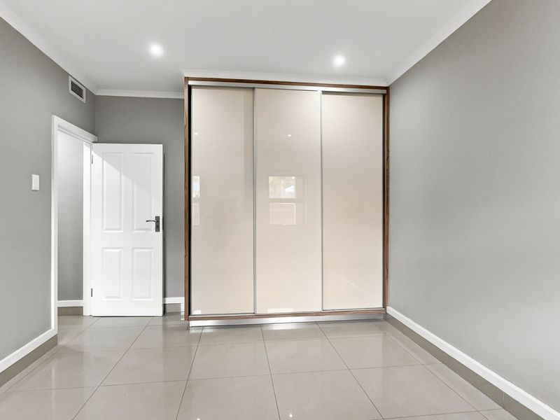 A clean, modern bedroom featuring neutral grey walls, large format floor tiles, and a sleek built-in sliding door wardrobe.