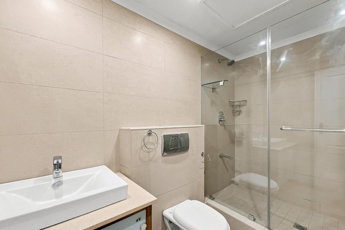Modern bathroom featuring a glass-enclosed shower, wall-mounted toilet, and a sleek basin set on a vanity countertop with neutral wall tiling.