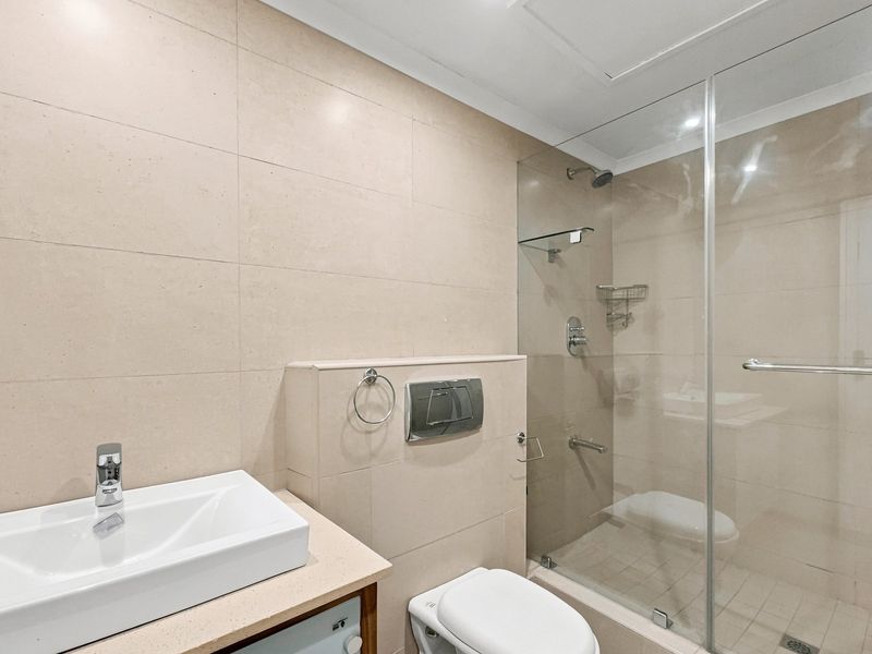 Modern bathroom featuring a glass-enclosed shower, wall-mounted toilet, and a sleek basin set on a vanity countertop with neutral wall tiling.