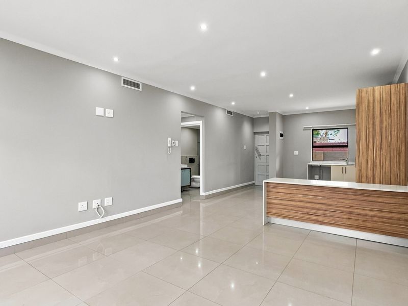 A bright, open-plan living and kitchen area featuring modern porcelain floor tiles, recessed downlighting, and contemporary wood-finish cabinetry.