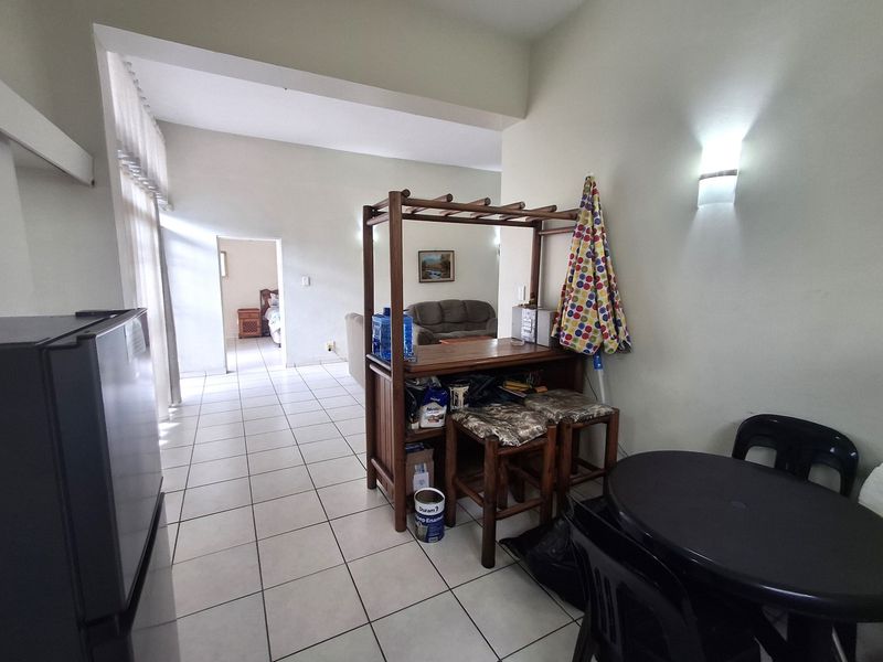 Open plan living area featuring neutral tiled flooring and wall-mounted lighting, providing a functional layout with access to adjacent rooms.