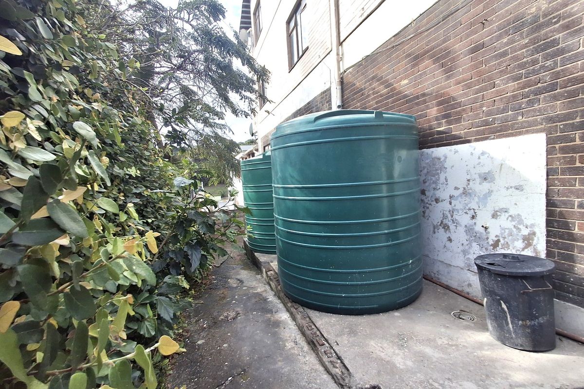 Rear exterior area featuring large water storage tanks positioned against a brick building facade with a concrete pathway.