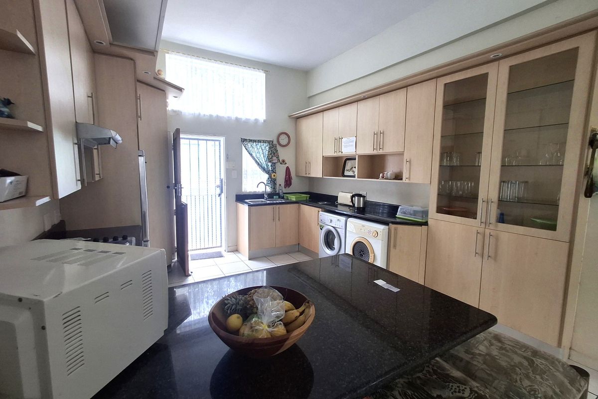 A functional kitchen featuring light wood cabinetry, granite countertops, integrated laundry appliances, and a central island, with direct access to an exterior door.