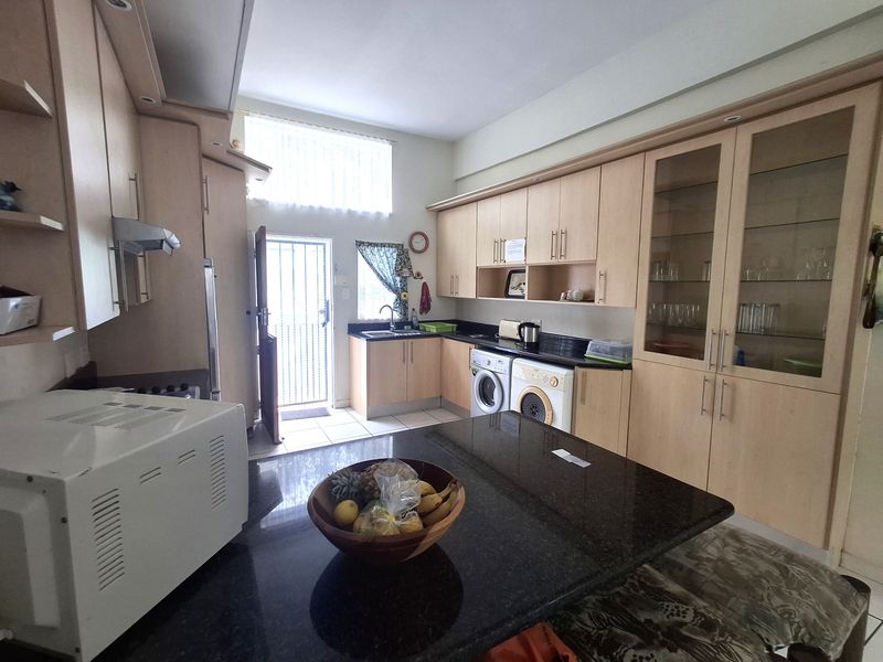 A functional kitchen featuring light wood cabinetry, granite countertops, integrated laundry appliances, and a central island, with direct access to an exterior door.