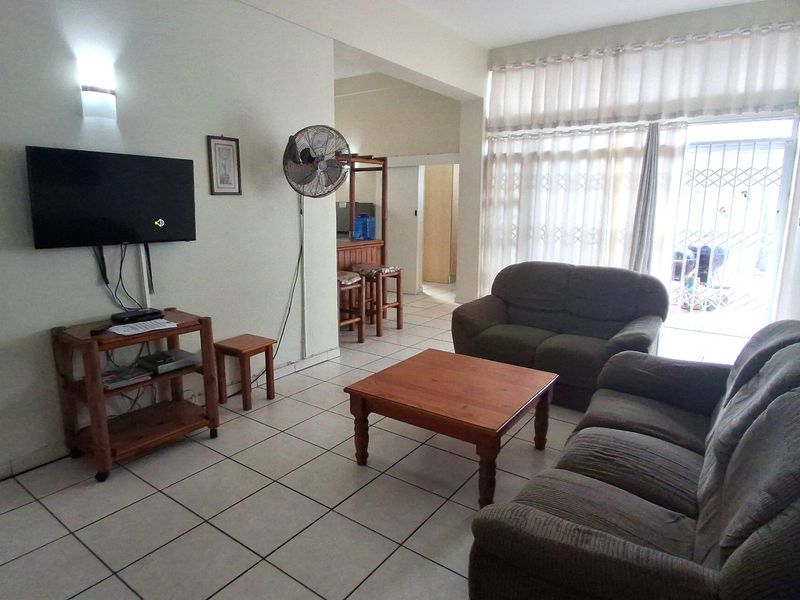 A living room featuring tiled flooring and a sliding glass door with security gate, providing access to the exterior area.