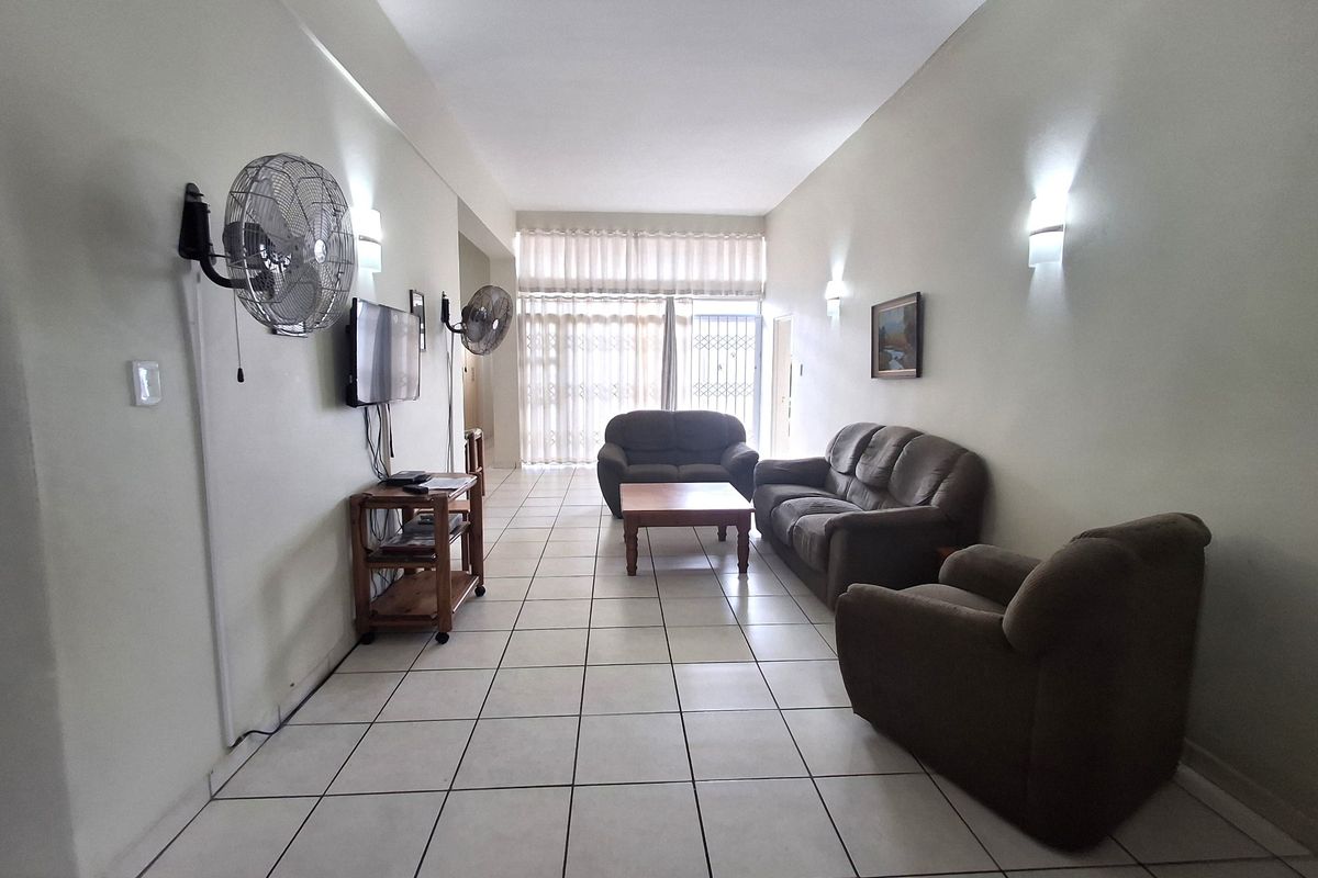 Spacious living room featuring ceramic floor tiles, wall-mounted lighting, and a sliding glass door leading to an outdoor area with security gate.