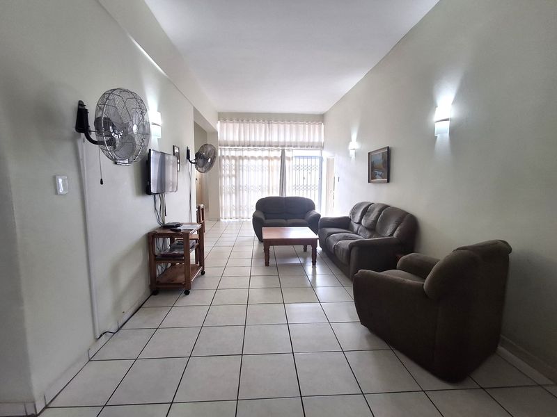 Spacious living room featuring ceramic floor tiles, wall-mounted lighting, and a sliding glass door leading to an outdoor area with security gate.