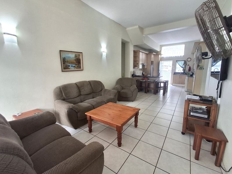 Open-plan living and kitchen area featuring tiled flooring, neutral walls, and a functional kitchen layout with a breakfast bar.