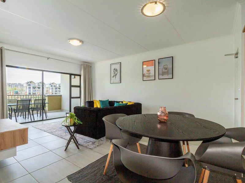 Bright open-plan living and dining area featuring tiled floors, flush mount lighting, and large sliding glass doors leading to a private balcony.