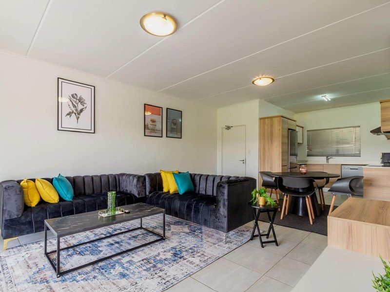 An open-plan living and kitchen area featuring tiled flooring, modern cabinetry, and integrated kitchen fixtures in a well-maintained apartment setting.