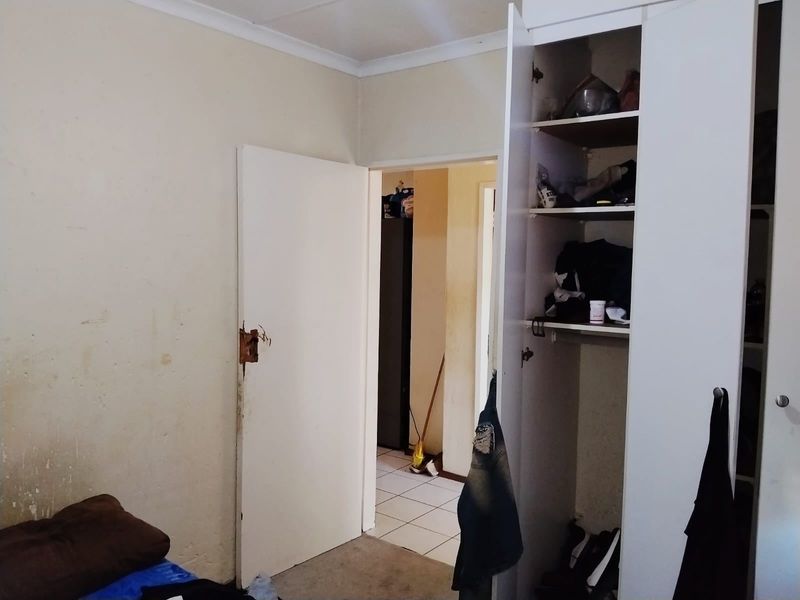 A bedroom featuring a built-in wardrobe and access to a hallway. The room requires cosmetic updates including wall repairs and fresh paint.