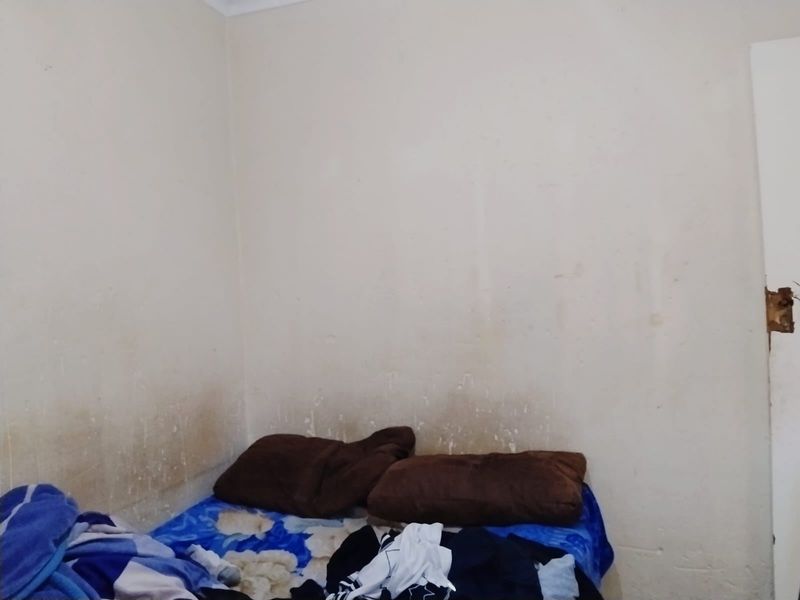 A bedroom interior featuring plain walls with visible surface staining and wear, requiring cosmetic attention and repainting.
