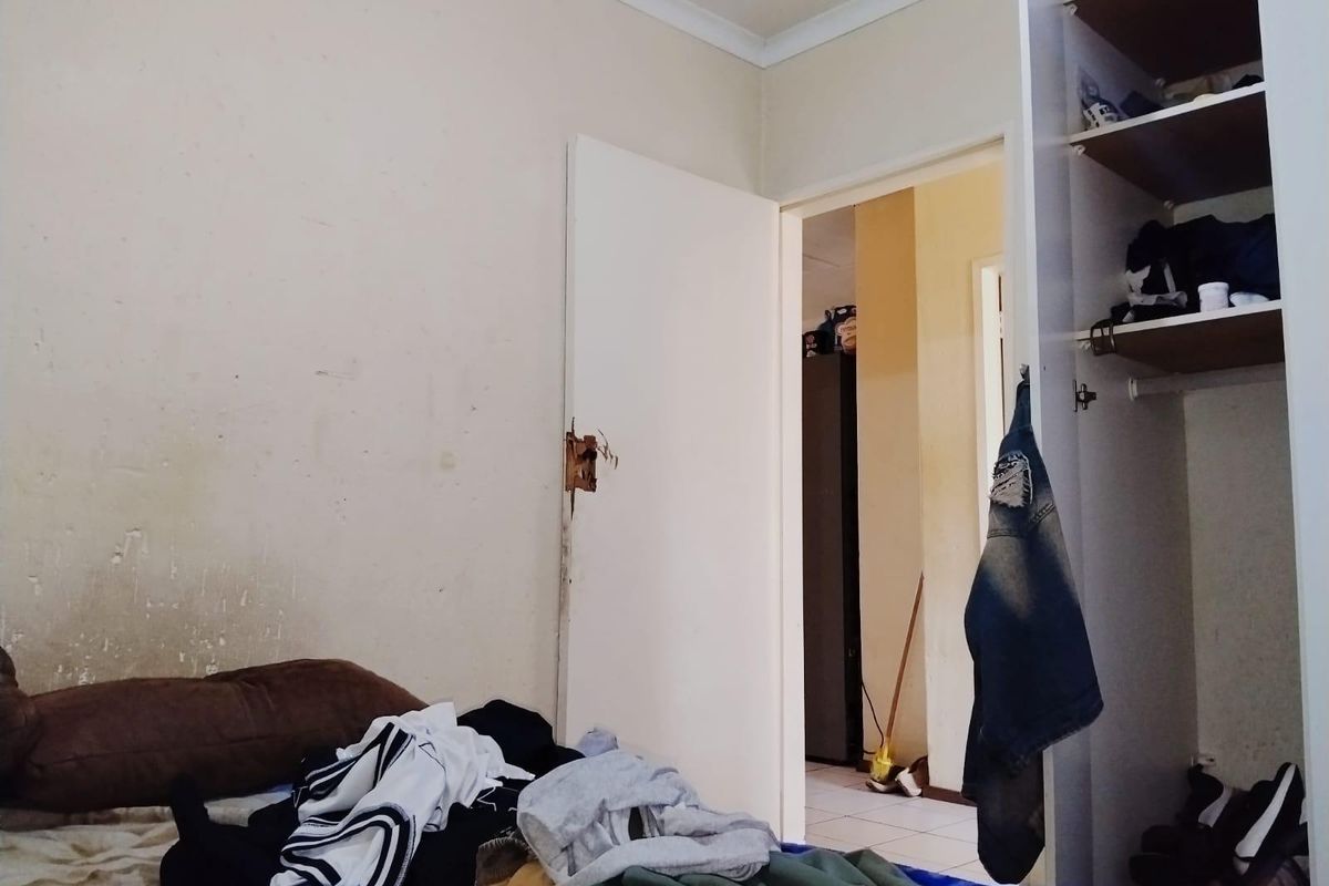 A bedroom featuring a built-in wardrobe and coving, showing signs of wear on the walls and door hardware.