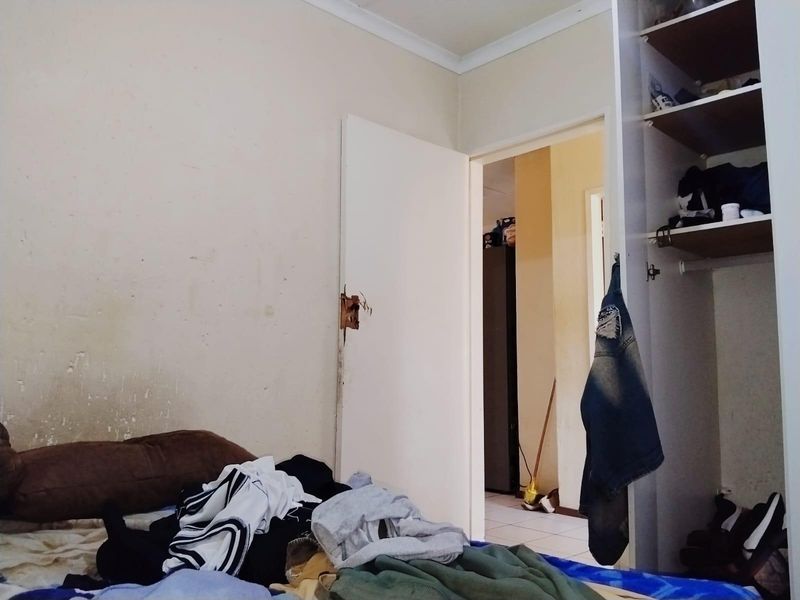 A bedroom featuring a built-in wardrobe and coving, showing signs of wear on the walls and door hardware.