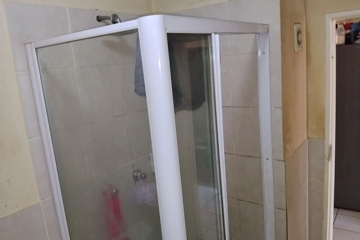A functional bathroom featuring a corner shower enclosure with tiled walls and flooring, currently showing signs of wear and requiring cosmetic updates.