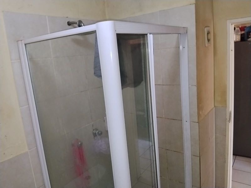 A functional bathroom featuring a corner shower enclosure with tiled walls and flooring, currently showing signs of wear and requiring cosmetic updates.