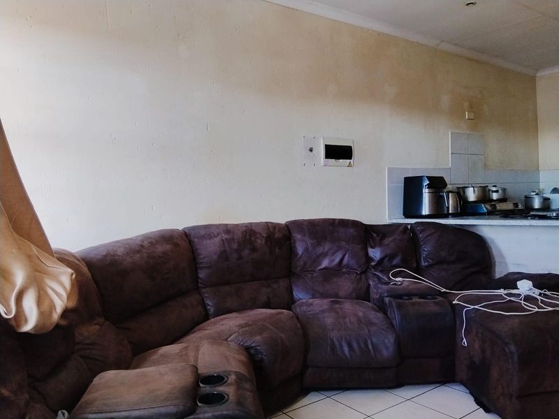 Open plan living area featuring tiled flooring and a kitchen corner with backsplash tiling, showing signs of wall discoloration and wear.