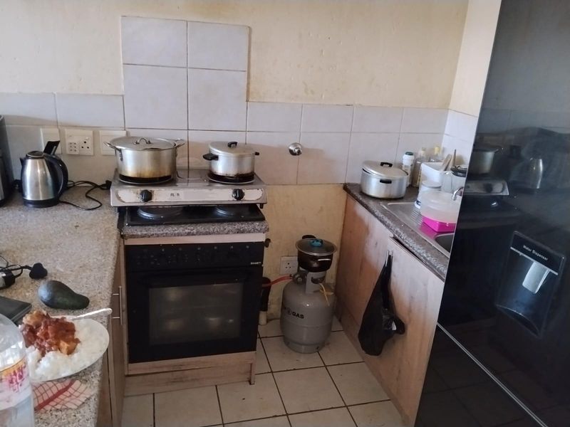 Compact kitchen featuring granite countertops, built-in oven, gas hob, and tiled backsplash. The space requires cosmetic updates to improve its overall condition.
