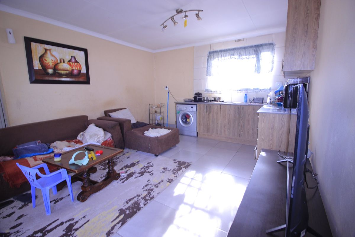 Open plan living area featuring tiled flooring and a compact kitchen corner with built-in cabinetry and sink.