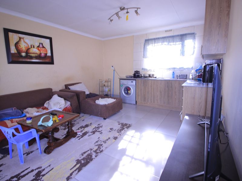 Open plan living area featuring tiled flooring and a compact kitchen corner with built-in cabinetry and sink.