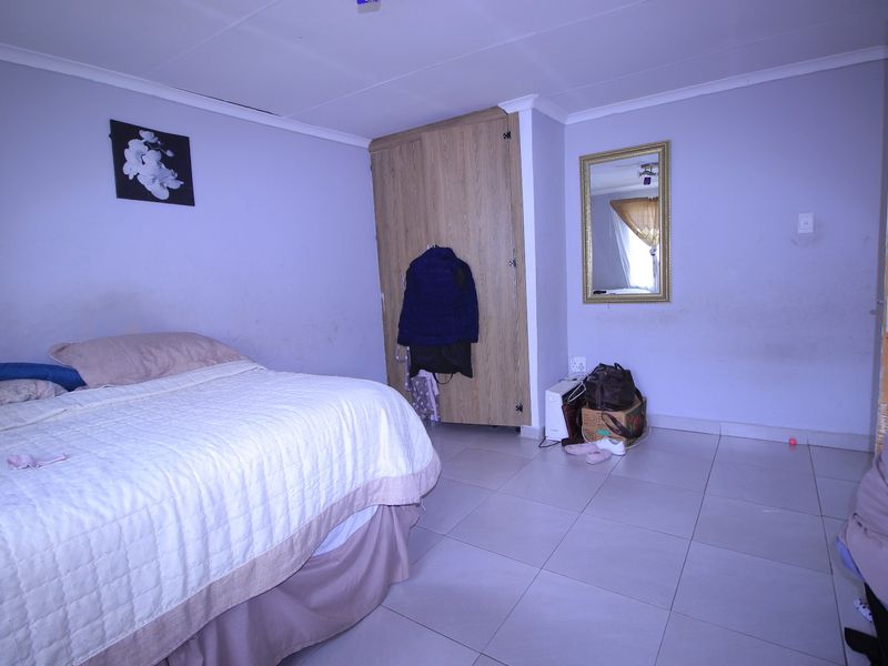A bedroom featuring tiled flooring, a built-in wardrobe, and coved ceilings. The walls show signs of wear and require maintenance.
