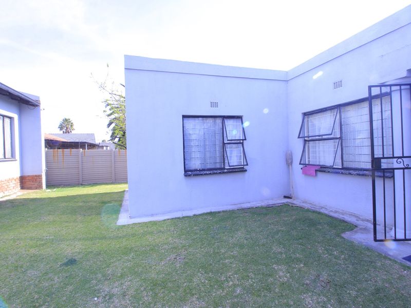 Rear exterior view of the property featuring a small lawn area, security bars on windows, and a security gate.
