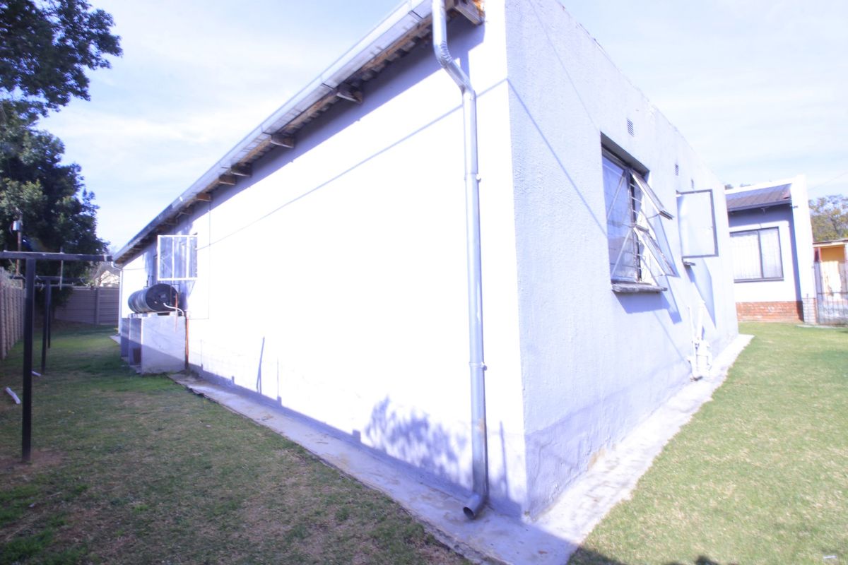 Rear exterior view of the property featuring a concrete apron, steel-framed windows, and an external water heater unit.