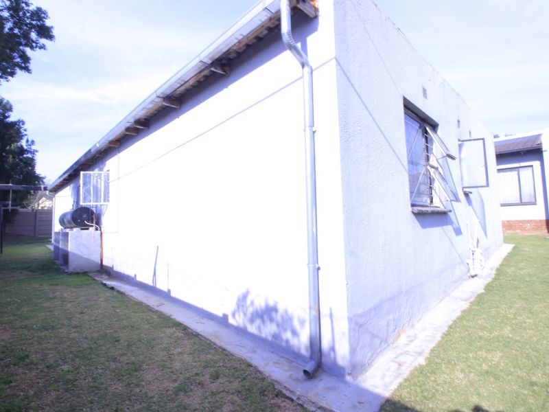 Rear exterior view of the property featuring a concrete apron, steel-framed windows, and an external water heater unit.