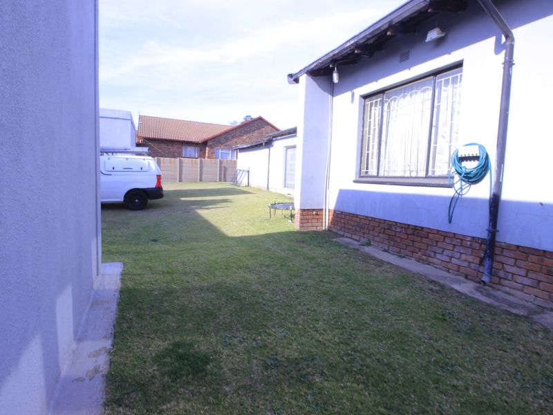 A view of the rear garden area featuring a lawn, brick plinth foundation, and security bars on the windows.
