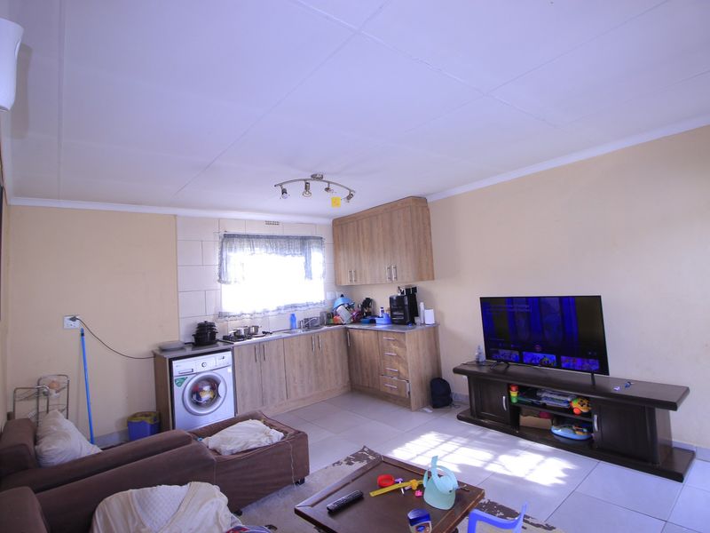 Open plan living area featuring a compact kitchen with built-in cabinetry, tiled flooring, and a wall-mounted air conditioning unit.