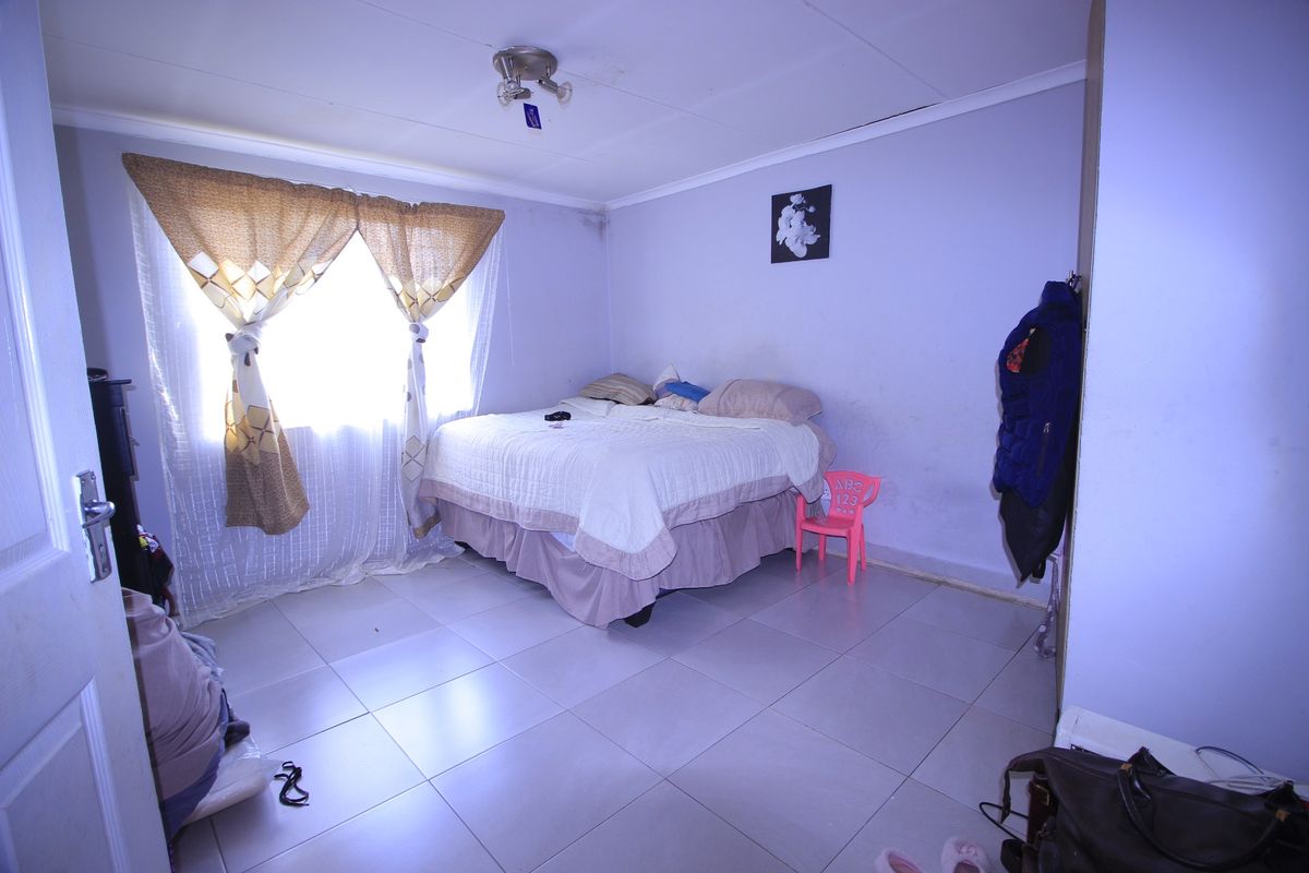A bedroom featuring tiled flooring, a ceiling light fixture, and built-in storage, currently showing signs of wear on the walls and ceiling.