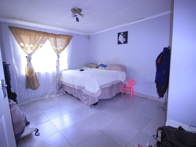 A bedroom featuring tiled flooring, a ceiling light fixture, and built-in storage, currently showing signs of wear on the walls and ceiling.