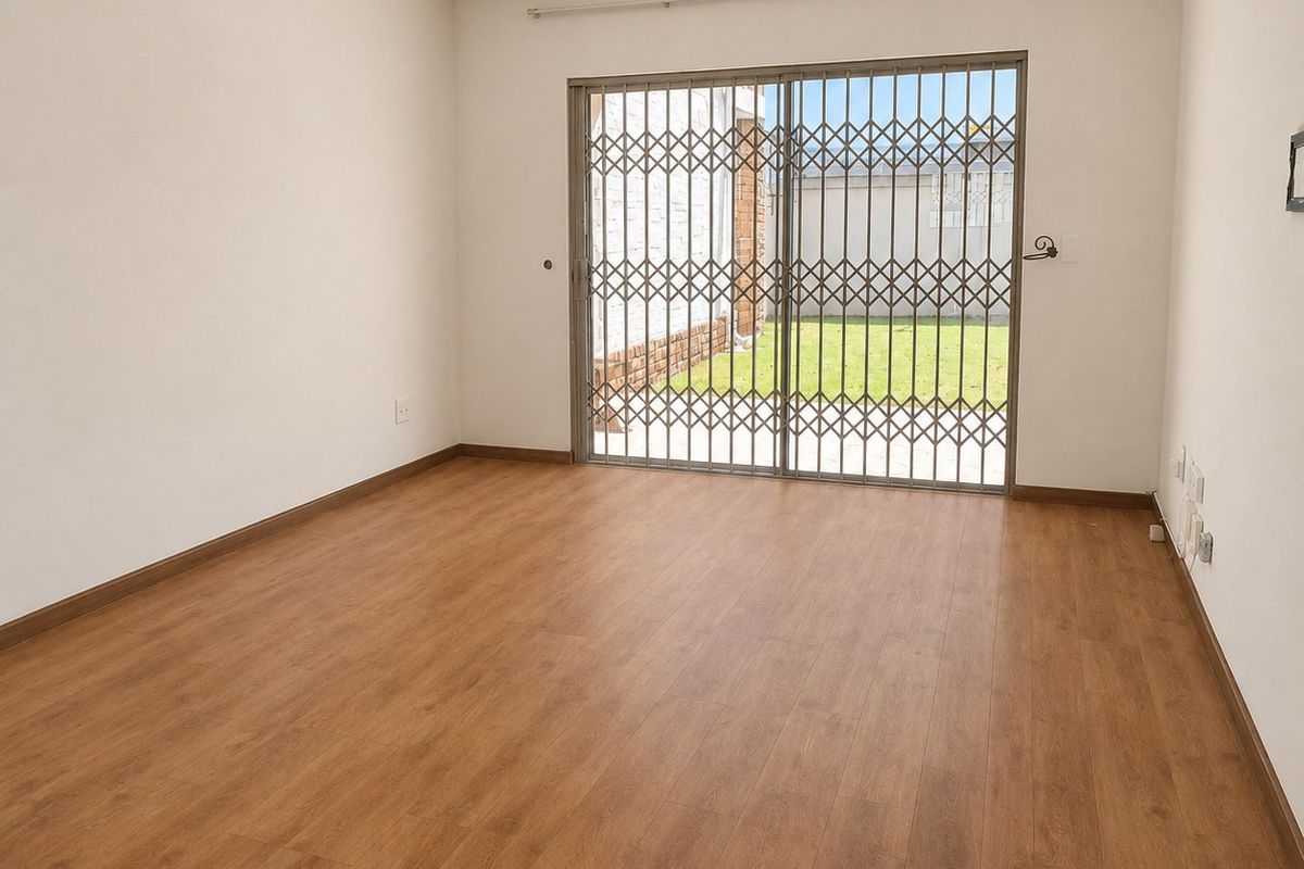 An empty, well-maintained living room featuring laminate flooring, recessed lighting, and a sliding glass door with a security gate leading to the garden.