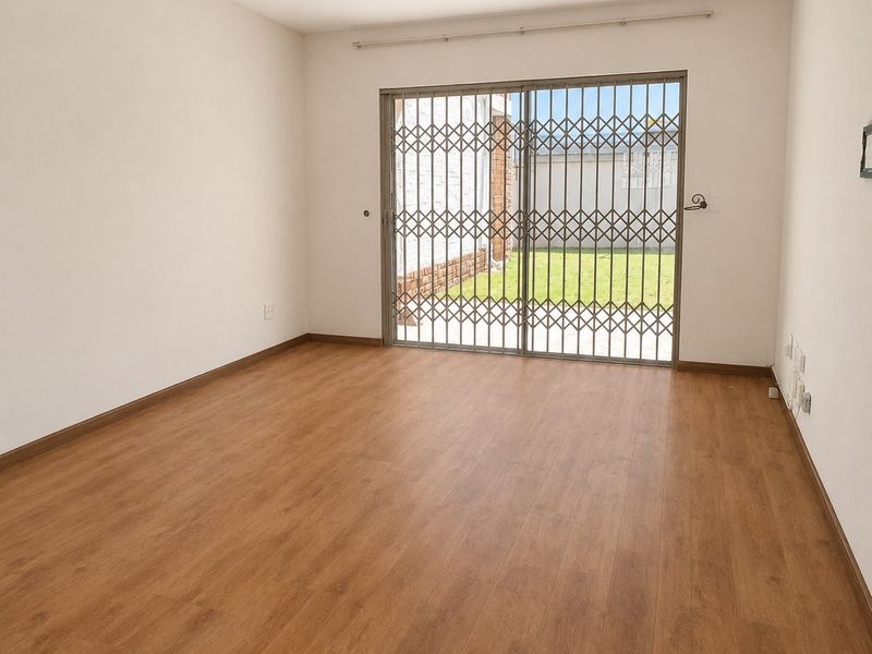 An empty, well-maintained living room featuring laminate flooring, recessed lighting, and a sliding glass door with a security gate leading to the garden.