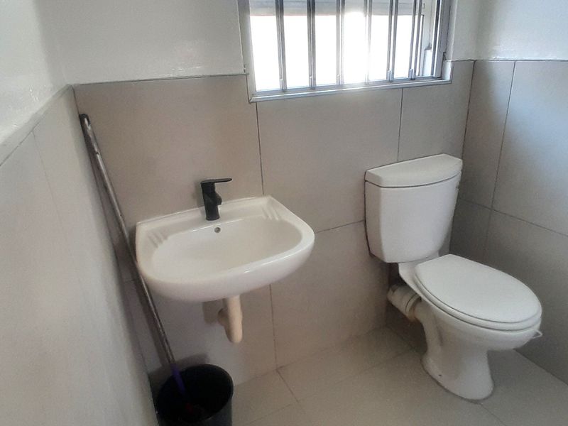 A compact bathroom featuring a wall-mounted basin, a standard toilet, and neutral wall tiling with a security gate over the window.