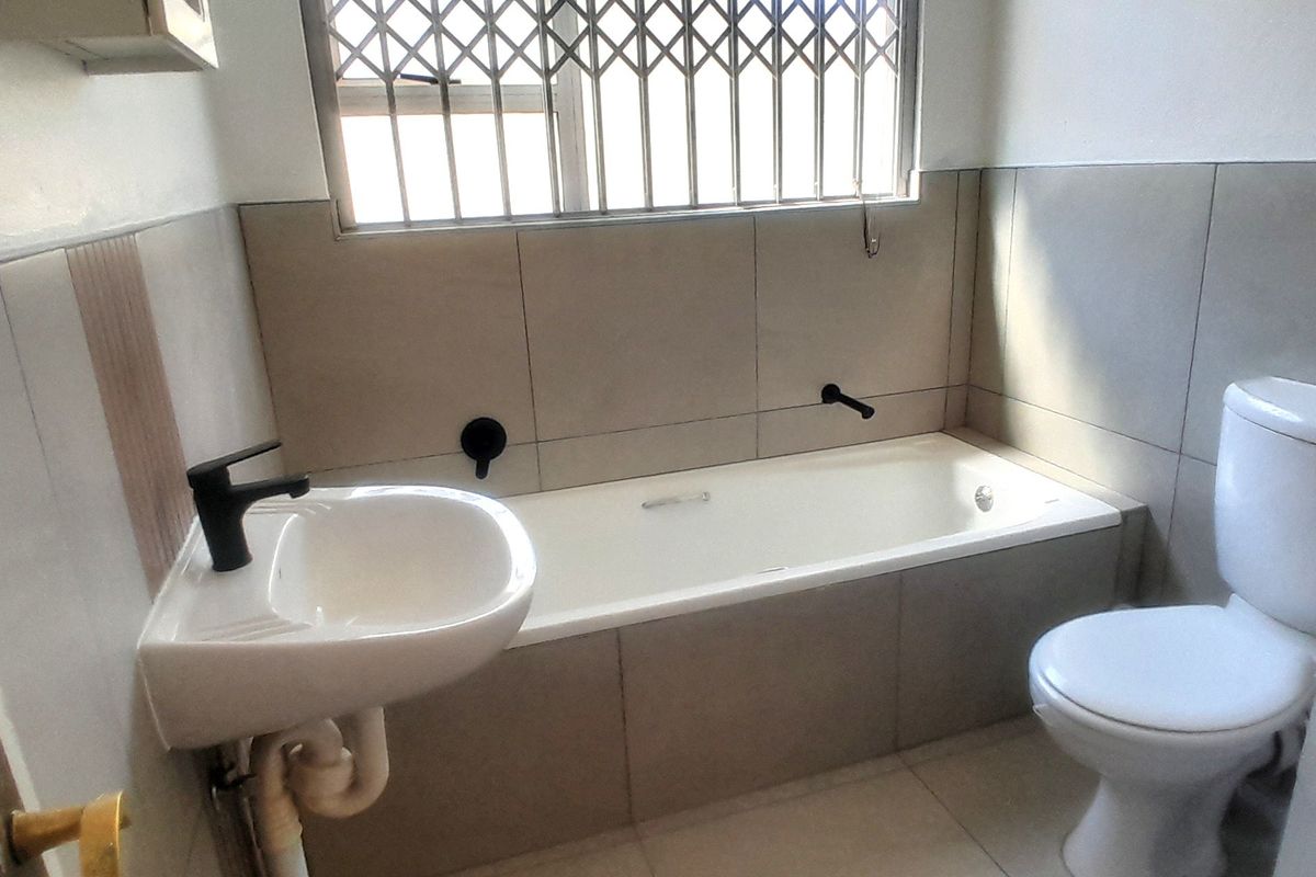 A functional bathroom featuring a bathtub, wall-mounted basin, and toilet with neutral tiling and modern black tapware.