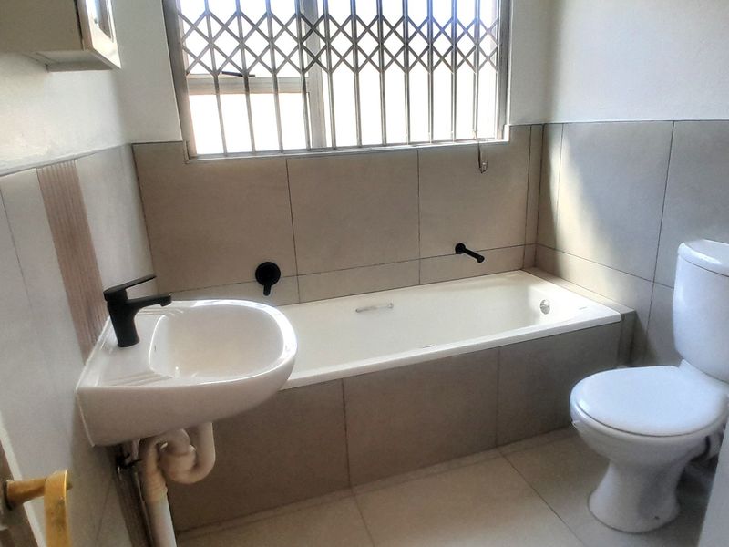 A functional bathroom featuring a bathtub, wall-mounted basin, and toilet with neutral tiling and modern black tapware.