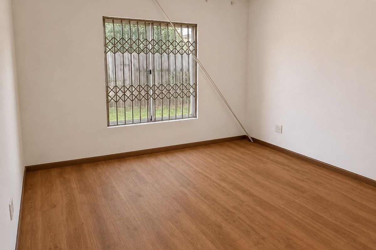 A bright, empty bedroom featuring wood-look laminate flooring, neutral walls, and a window fitted with security bars and a security gate.