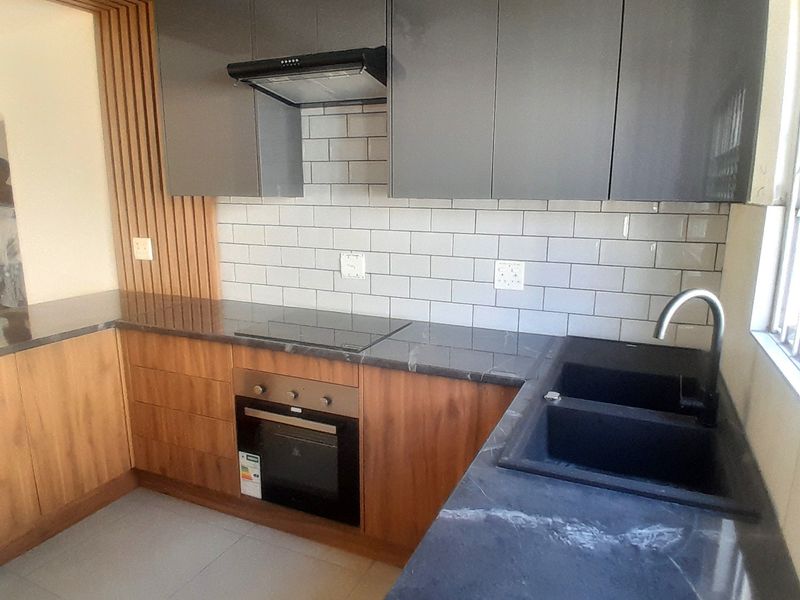 Modern kitchen featuring sleek grey and timber cabinetry, stone countertops, subway tile backsplash, and integrated appliances including an oven and hob.