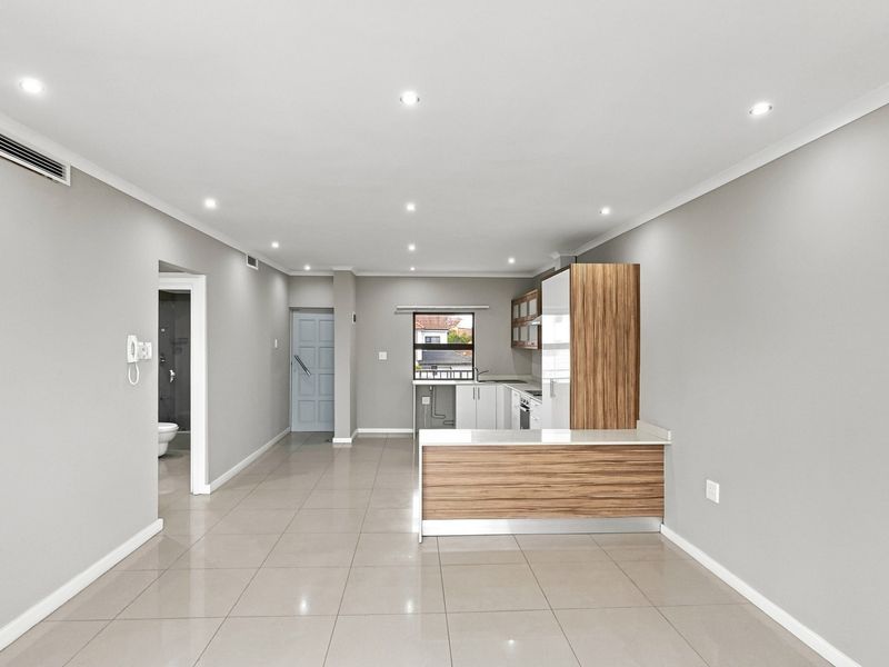 Modern open-plan living area featuring tiled flooring, recessed lighting, ducted air conditioning, and a contemporary kitchen with built-in appliances and stone countertops.