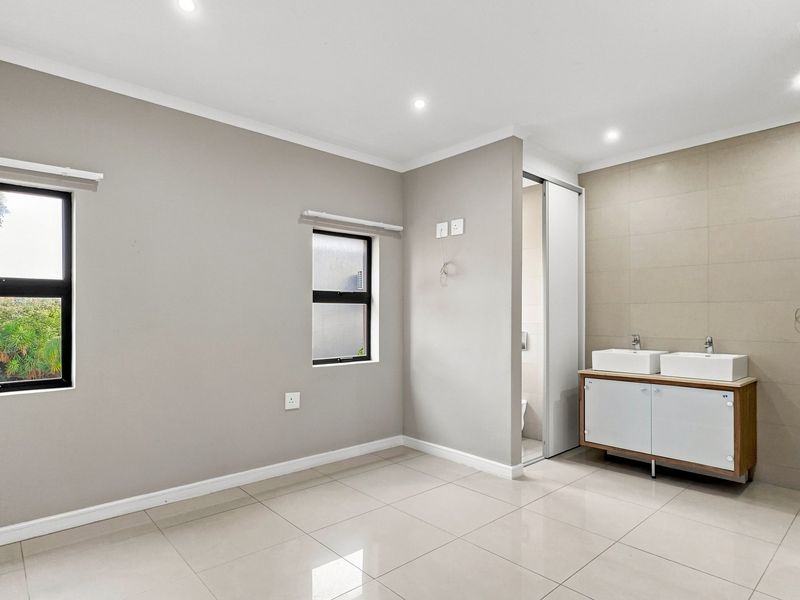 Spacious bedroom featuring neutral tiled flooring, recessed lighting, and an integrated double vanity with a tiled feature wall.