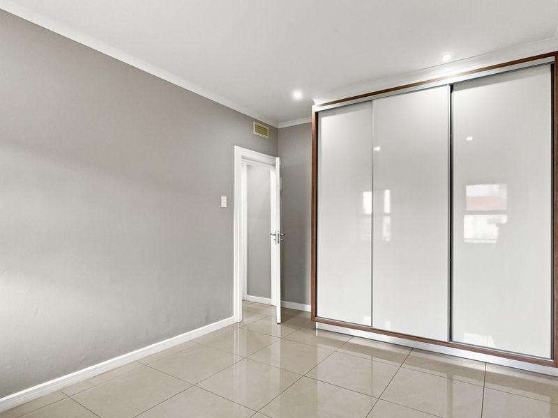 A bright, empty bedroom featuring modern tiled flooring, recessed downlights, and a large built-in wardrobe with white sliding doors.
