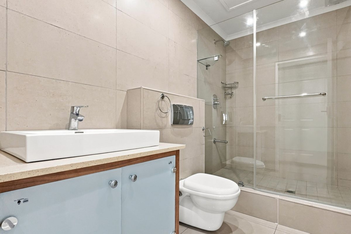 Modern bathroom featuring a wall-mounted toilet, glass-enclosed shower, and a contemporary vessel sink set on a vanity cabinet with neutral wall tiling.