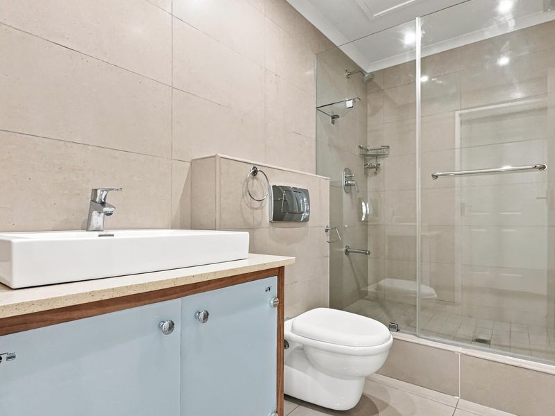 Modern bathroom featuring a wall-mounted toilet, glass-enclosed shower, and a contemporary vessel sink set on a vanity cabinet with neutral wall tiling.