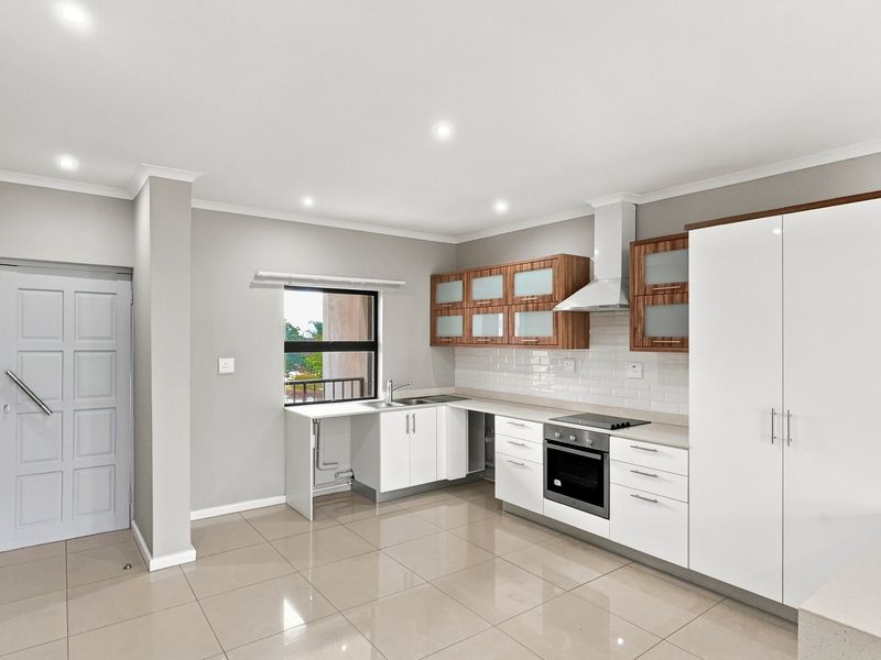 Modern kitchen featuring white and wood-tone cabinetry, subway tile backsplash, integrated oven and hob, and sleek tiled flooring in a bright, open space.