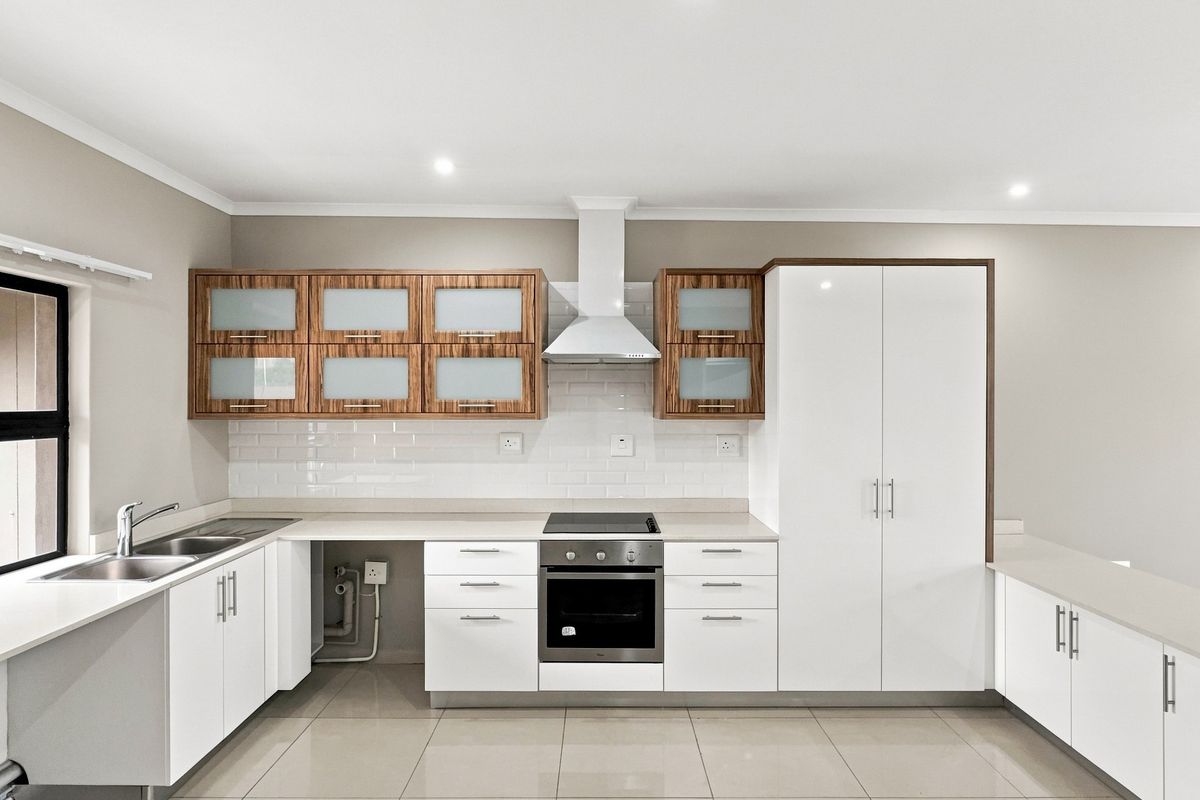 Modern kitchen featuring white cabinetry, wood-accented wall units, subway tile backsplash, built-in oven, electric hob, and sleek countertops in a clean, well-lit space.