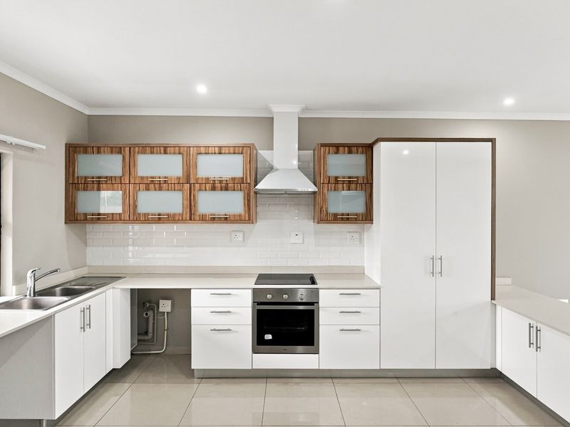 Modern kitchen featuring white cabinetry, wood-accented wall units, subway tile backsplash, built-in oven, electric hob, and sleek countertops in a clean, well-lit space.